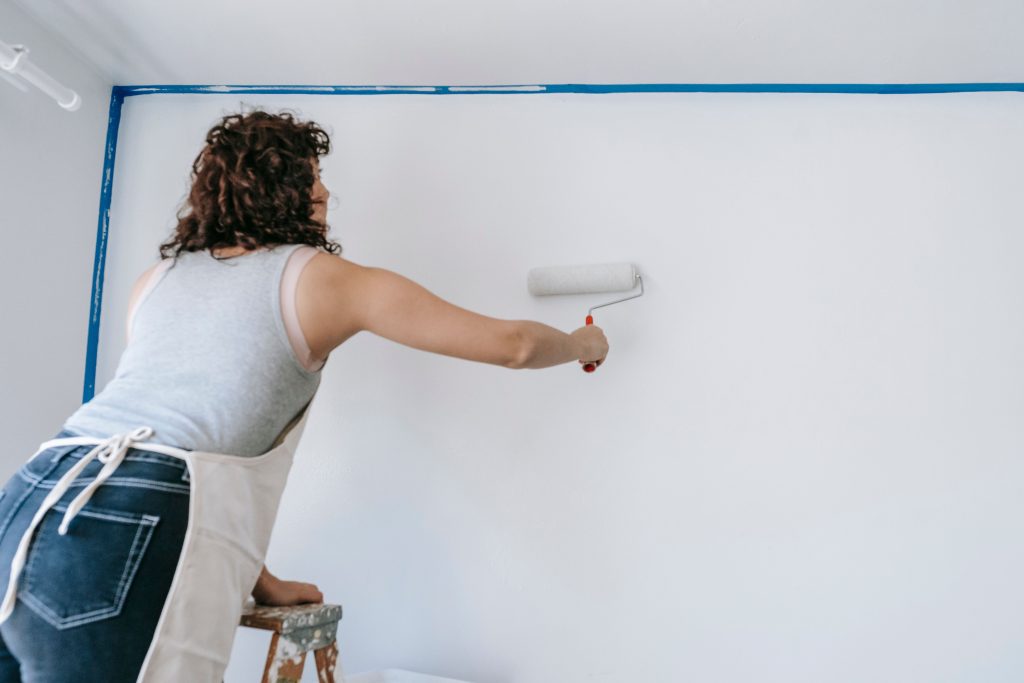 Peintre appliquant une peinture mate blanche au rouleau long manche sur un plafond à Douala